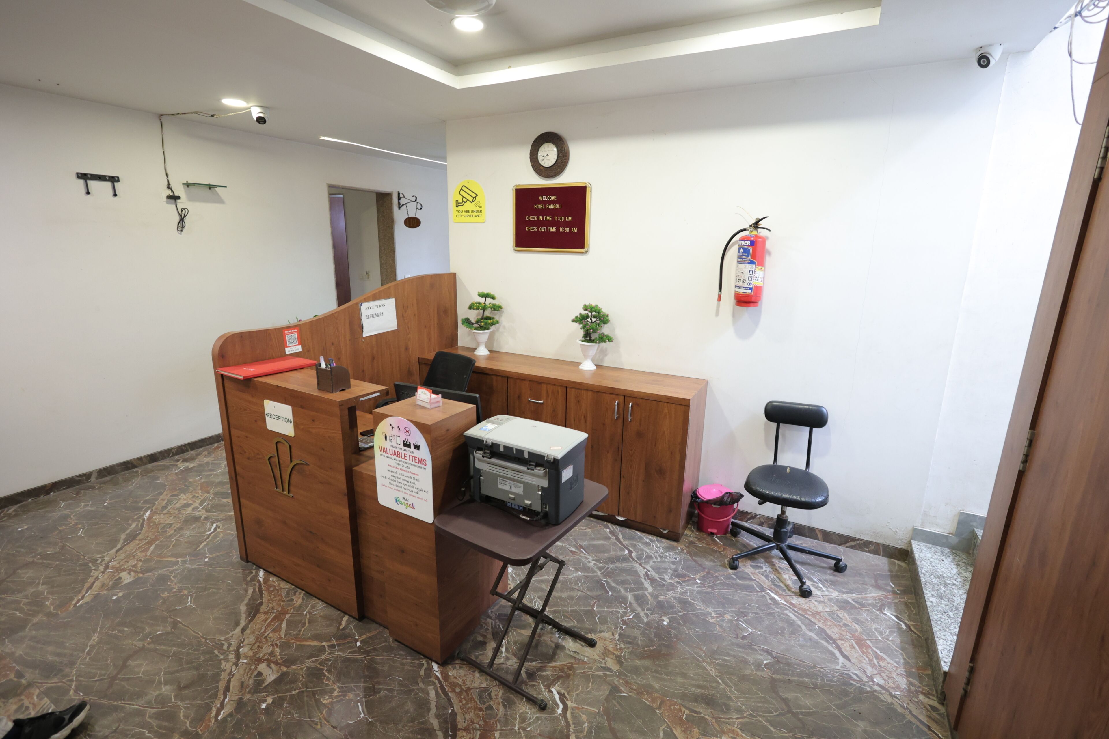 Un espace d’accueil comprenant un bureau en bois, une imprimante, un comptoir de réception, une horloge et un extincteur.