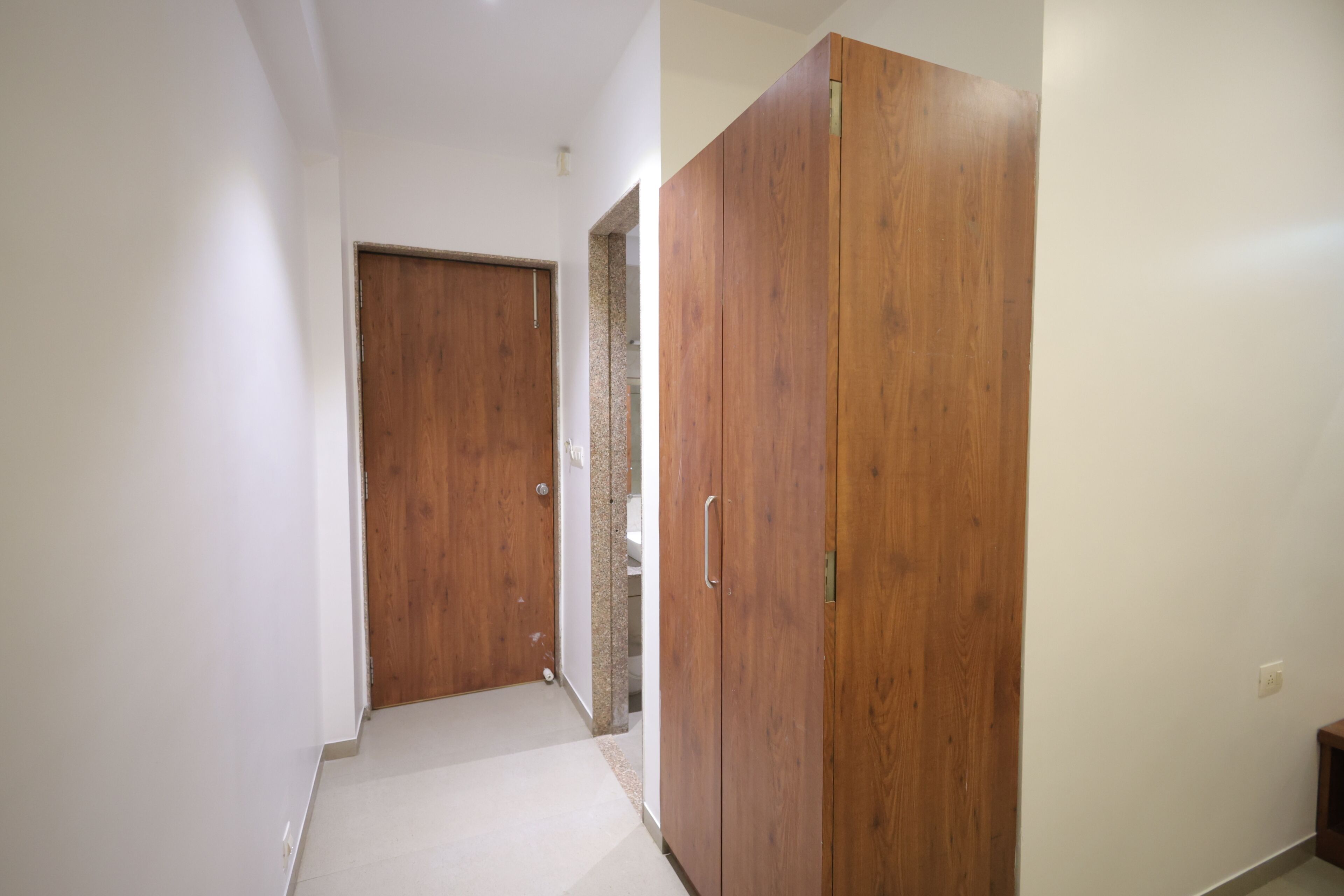 A hallway with a wooden wardrobe, a door, and a tiled wall.