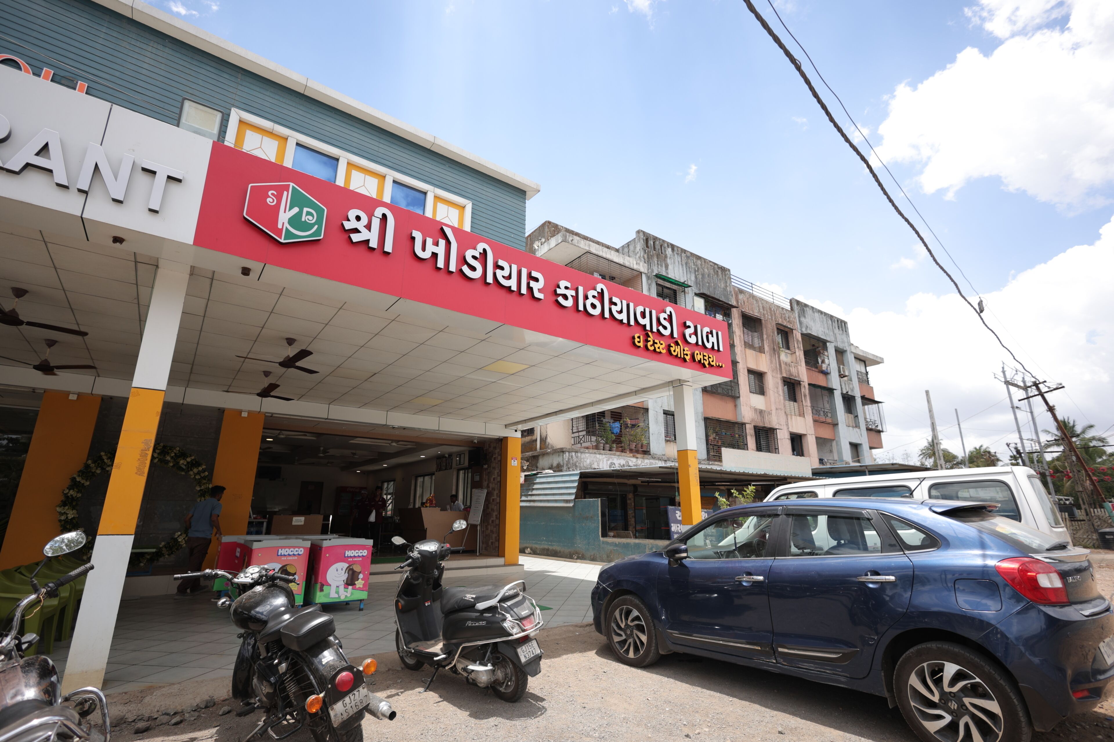 A building with a signboard, a parked car, and a motorcycle.