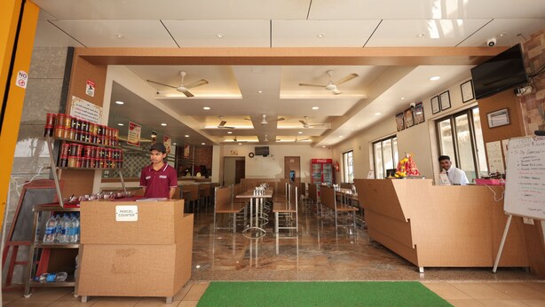 A hotel lobby with a reception desk, seating area, ceiling fans, and a Coca-Cola refrigerator.
