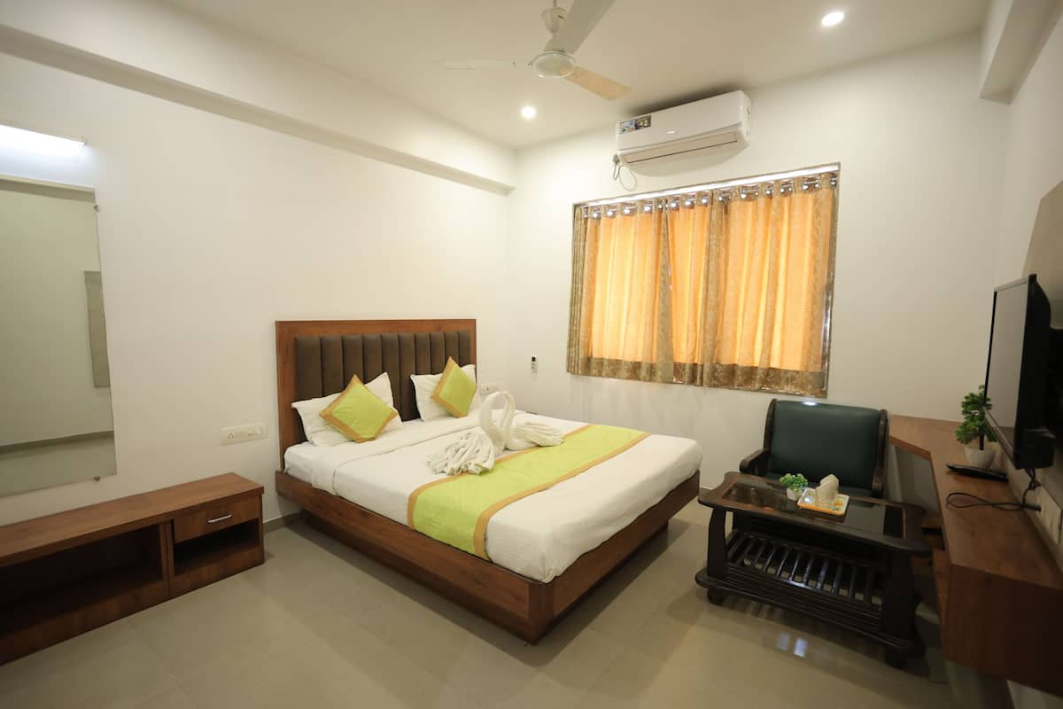 A hotel room with a bed, a desk, a chair, a TV, and a window with curtains.