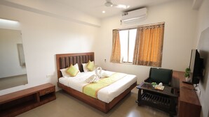 A hotel room with a bed, a desk, a chair, a TV, and an air conditioning unit.