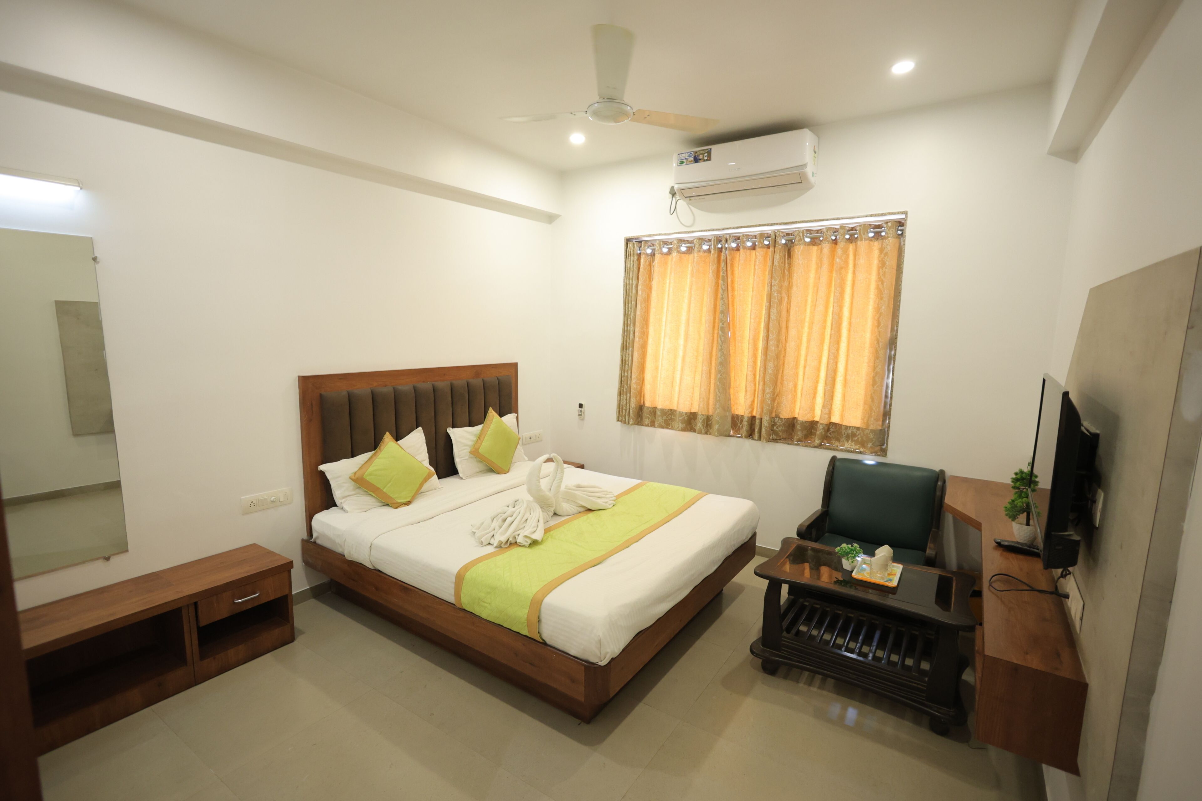 A hotel room with a bed, a desk, a chair, a TV, and an air conditioning unit.