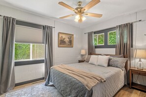 A bedroom with a bed, a ceiling fan, a window with curtains, a nightstand with a lamp, and a framed picture on the wall. - Hilltop Manhattan Retreat Near K-State w/ Laundry (Manhattan)