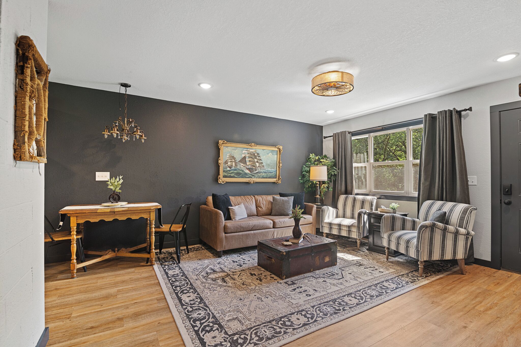 A living room with a dark wall, a chandelier, a sofa, armchairs, a coffee table, and a window with curtains.