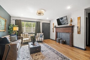 A living room with a sofa, armchairs, a coffee table, a fireplace, a TV, and a window with curtains. - Hilltop Manhattan Retreat Near K-State w/ Laundry (Manhattan)