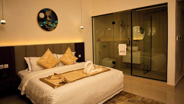 Habitación de hotel con cama, una obra de arte en la pared, un baño con mampara de vidrio y una mesita de noche de madera.