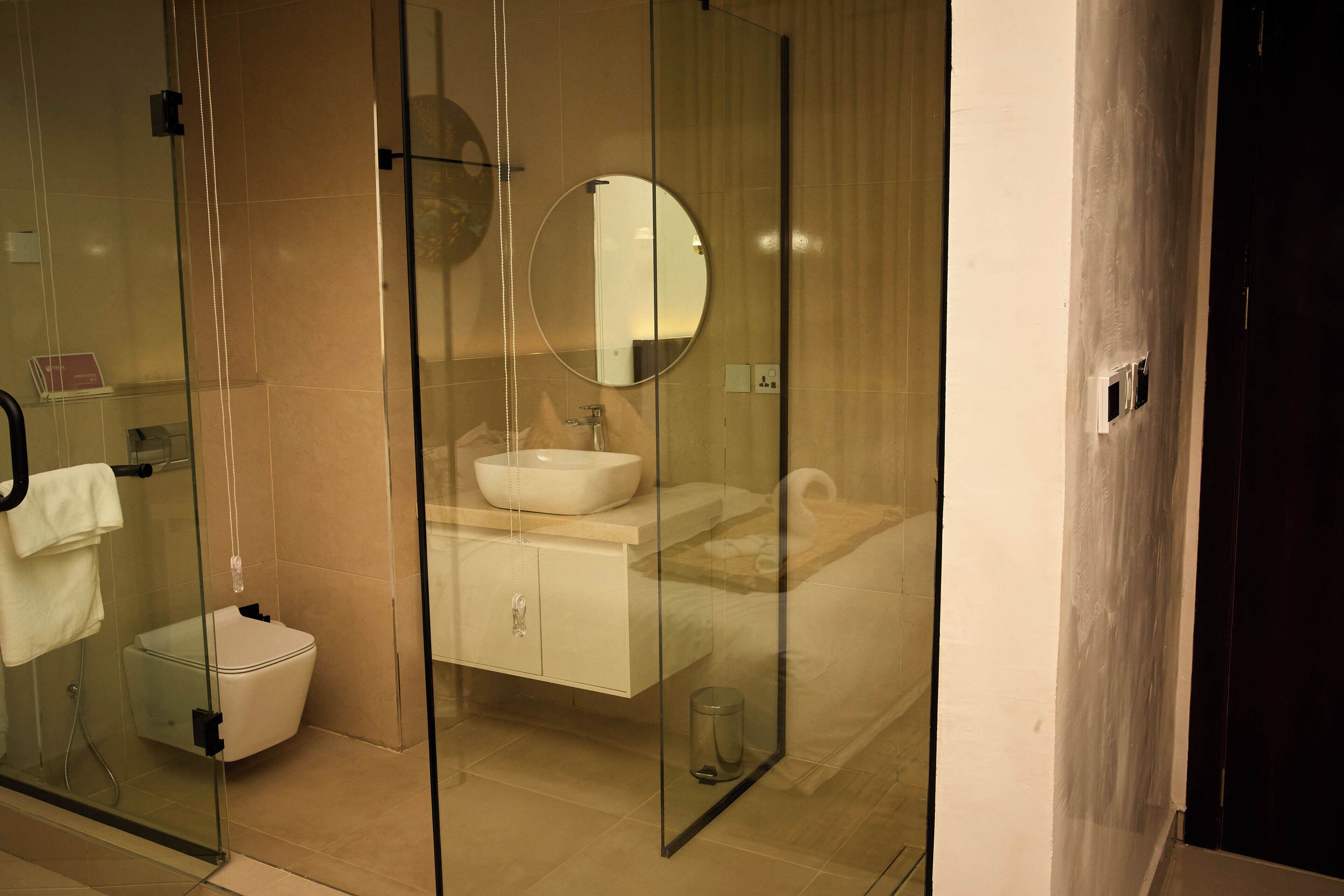A modern bathroom with a glass shower enclosure, a round mirror, a sink, and a toilet.