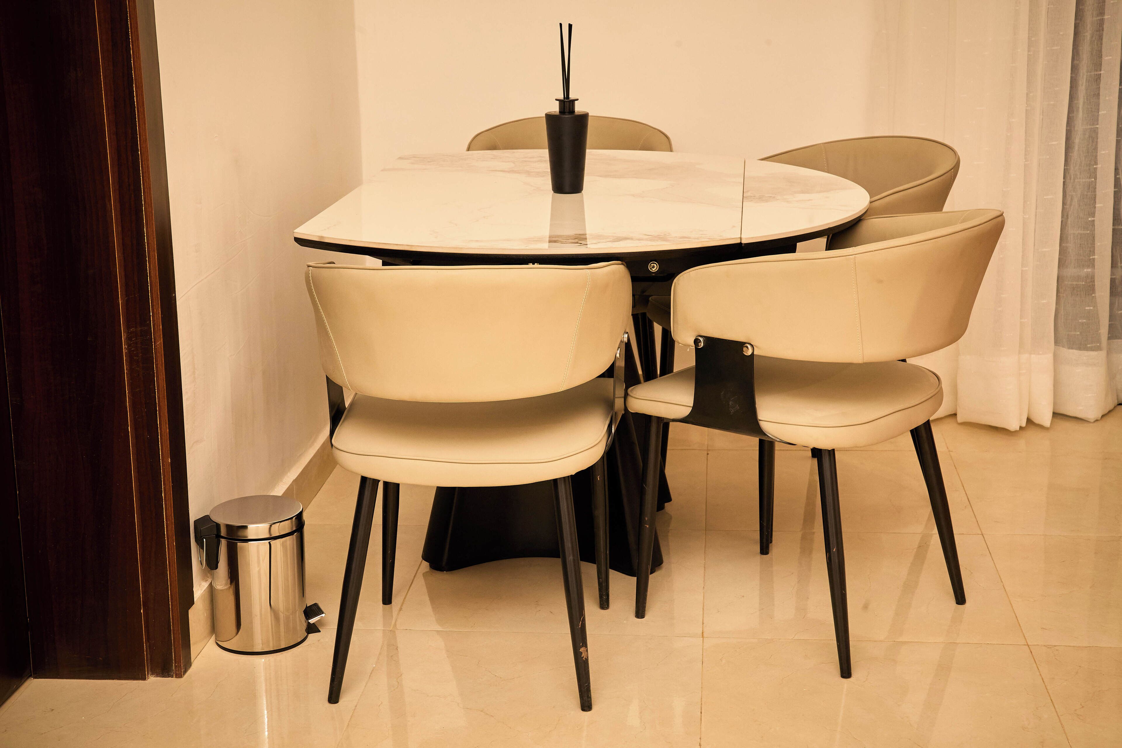 Un coin repas comprenant une table ronde, quatre chaises, une poubelle et une porte.