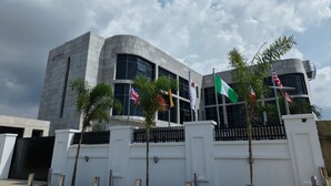 Un edificio moderno con fachada blanca, varias banderas y una entrada porticada.