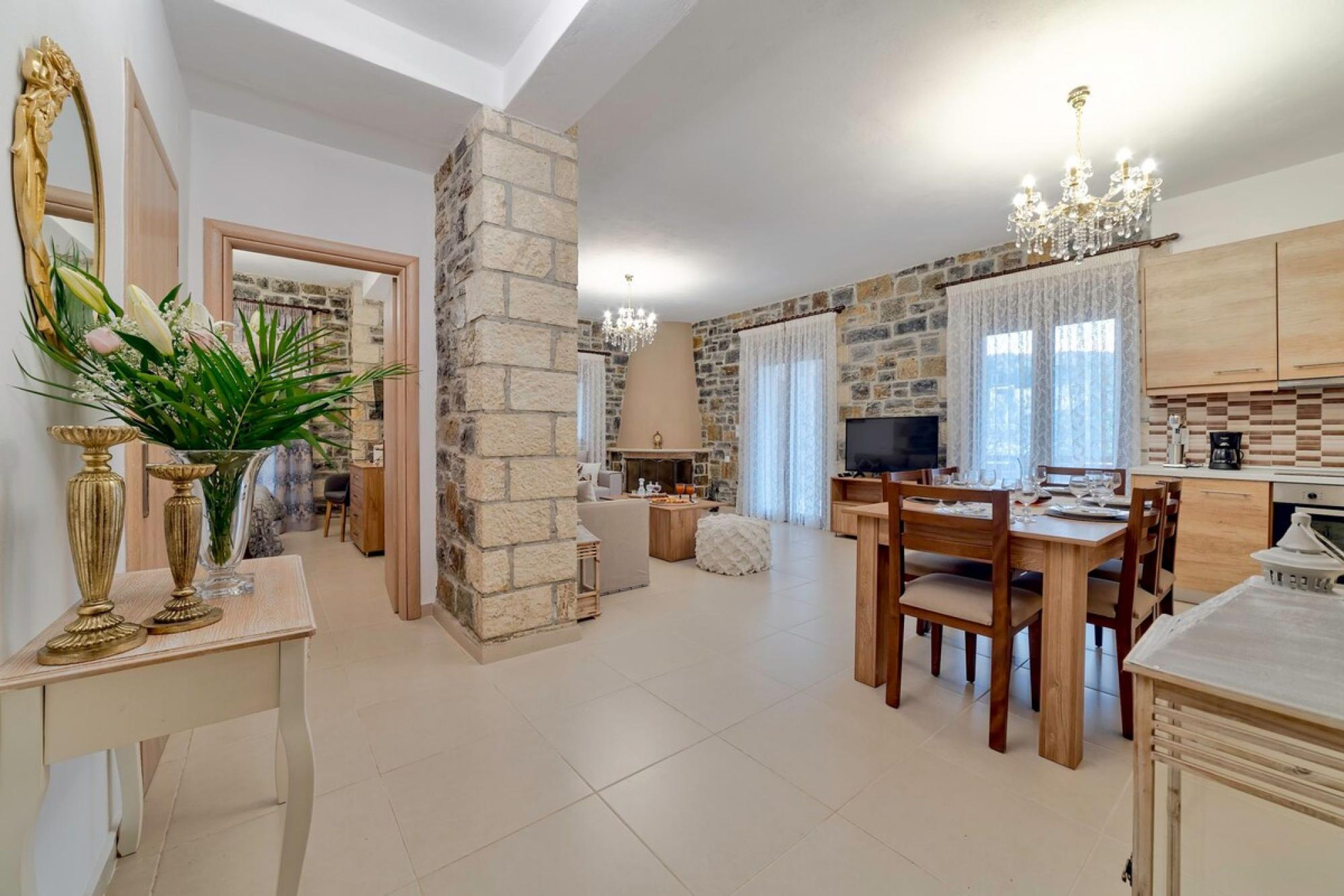 A spacious living area with a stone fireplace, a dining table set for four, and a kitchen with wooden cabinets and a chandelier.