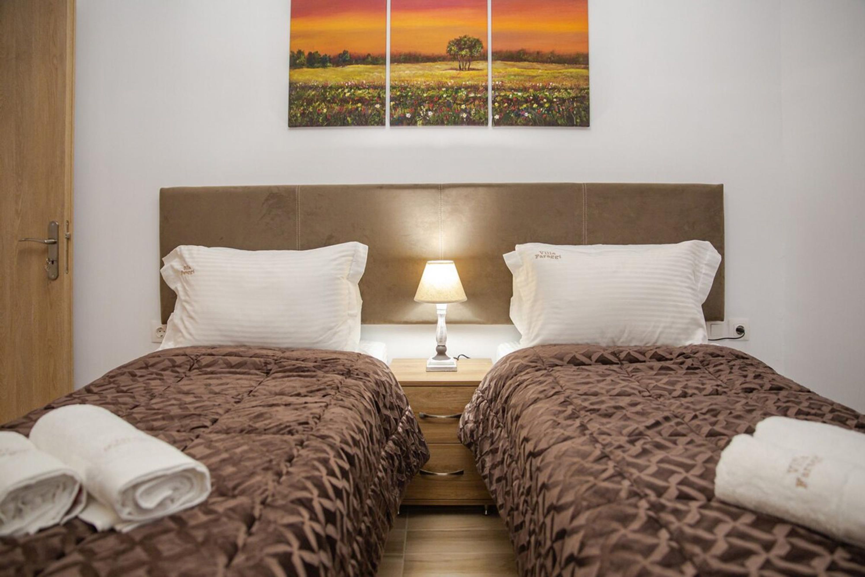 A double room with two beds, a nightstand with a lamp, and a wall-mounted painting.
