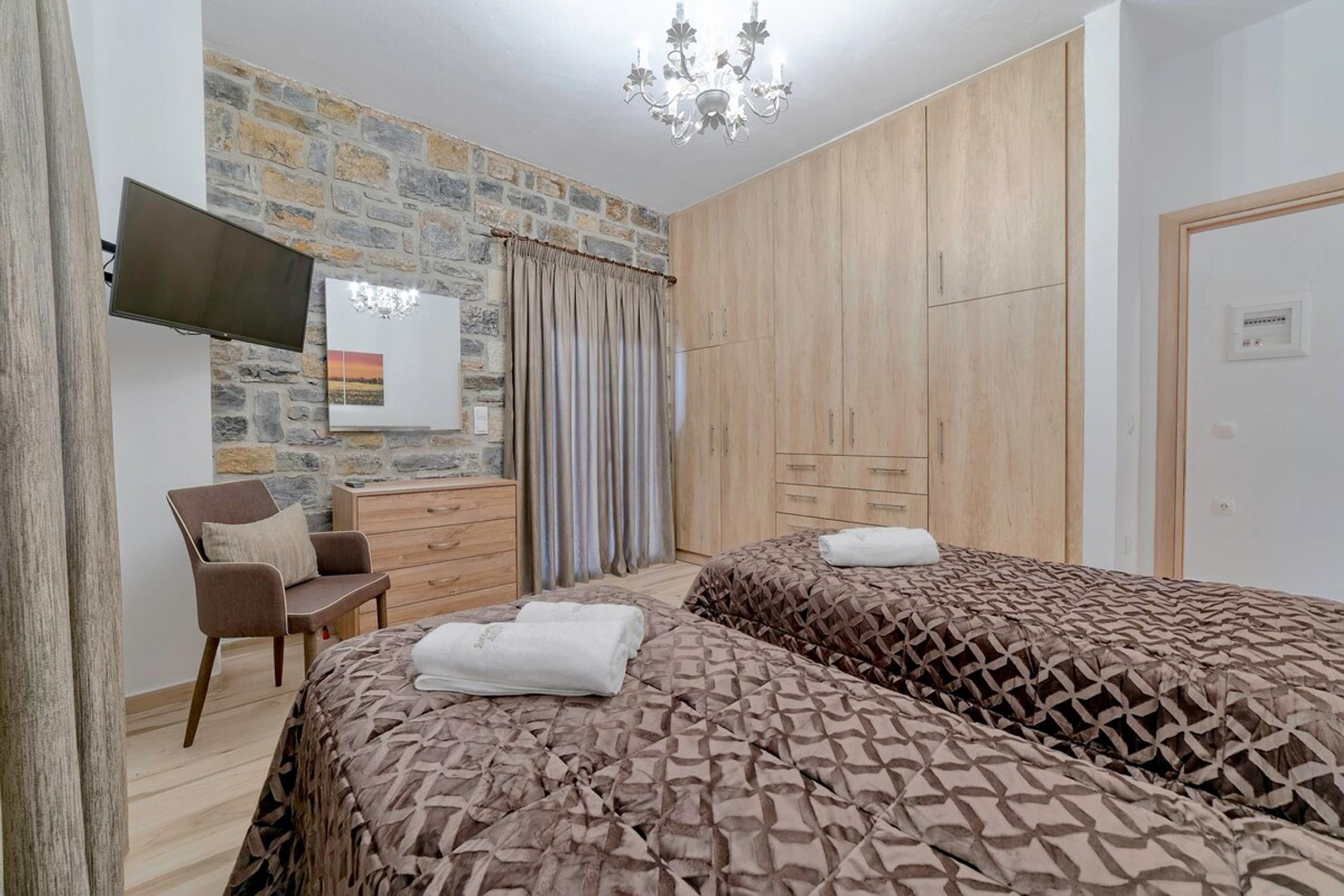 Une chambre avec deux lits, une télévision, un bureau et un mur en pierre.