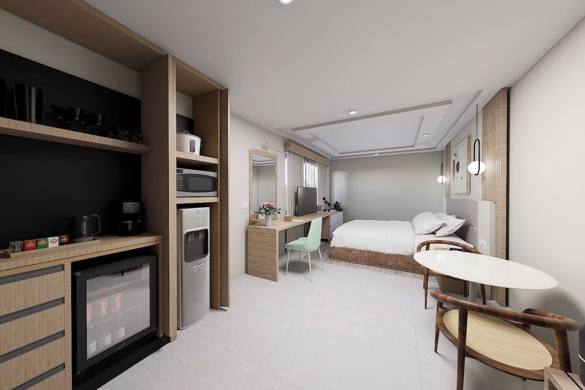 A compact hotel room with a kitchenette, a bed, a desk, and a small dining area.