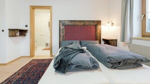 Una habitación de hotel con cama, mesita de noche, lámpara, ventana con cortinas y puerta que da a un baño.