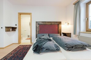 A hotel room with a bed, a nightstand, a lamp, a window with curtains, and a door leading to a bathroom. - Landhaus Stieglschuster – Apartment for 2 | 360° Mountain View | 5 Ski Areas (Irdning)