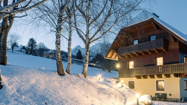 Una cabaña de madera con balcón, suelo cubierto de nieve y un farol.