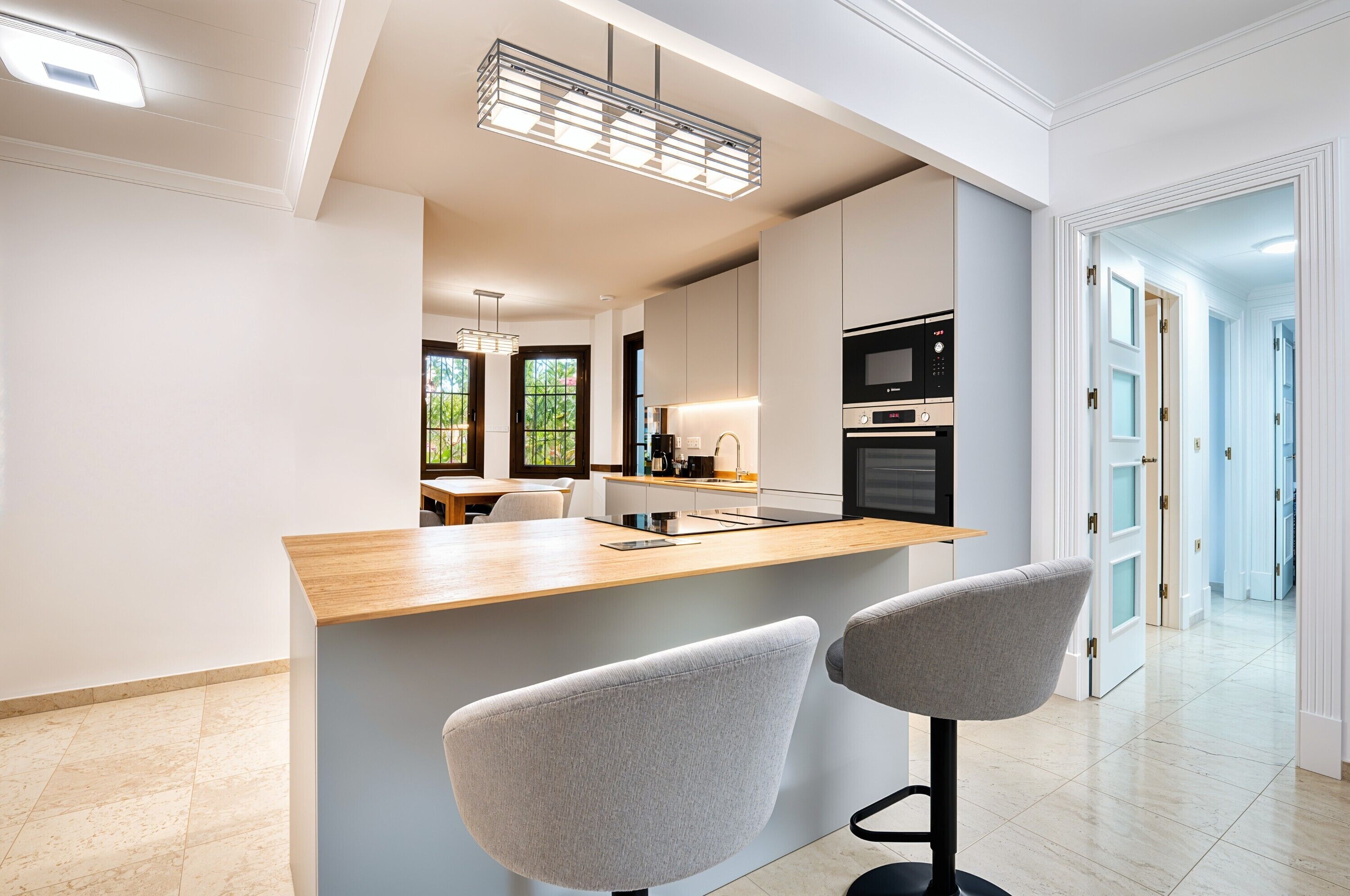A modern kitchen with a central island, bar stools, and a view into the dining area.