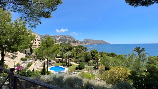 A coastal landscape with a swimming pool, lush greenery, and a clear blue sky. - Apartment 'Villa Gadea 7-1' with Shared Pool, Private Terrace and Wi-Fi (Villa Gadea urbanizacion)