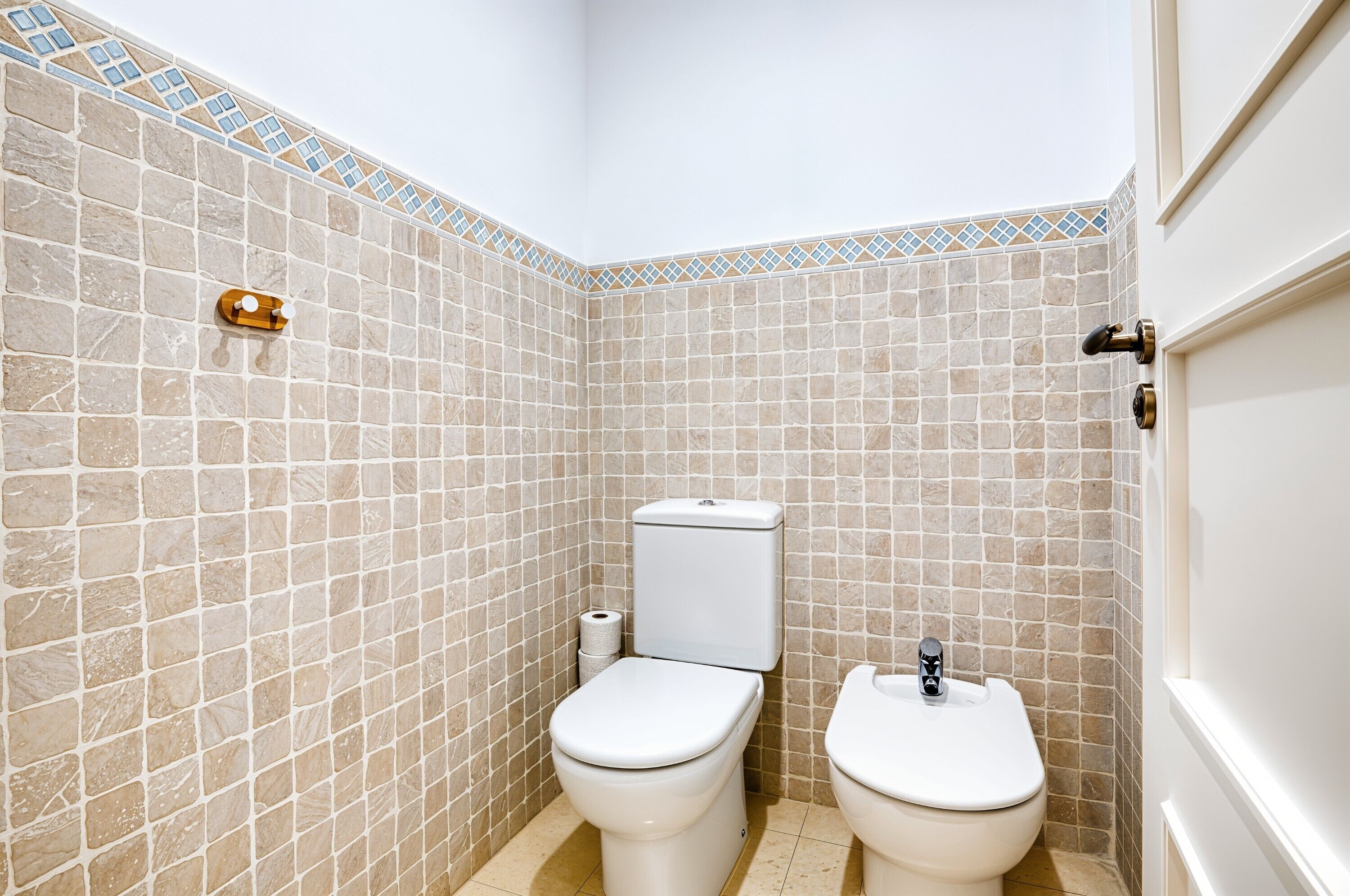 Un baño con dos inodoros, ducha y pared con azulejos.