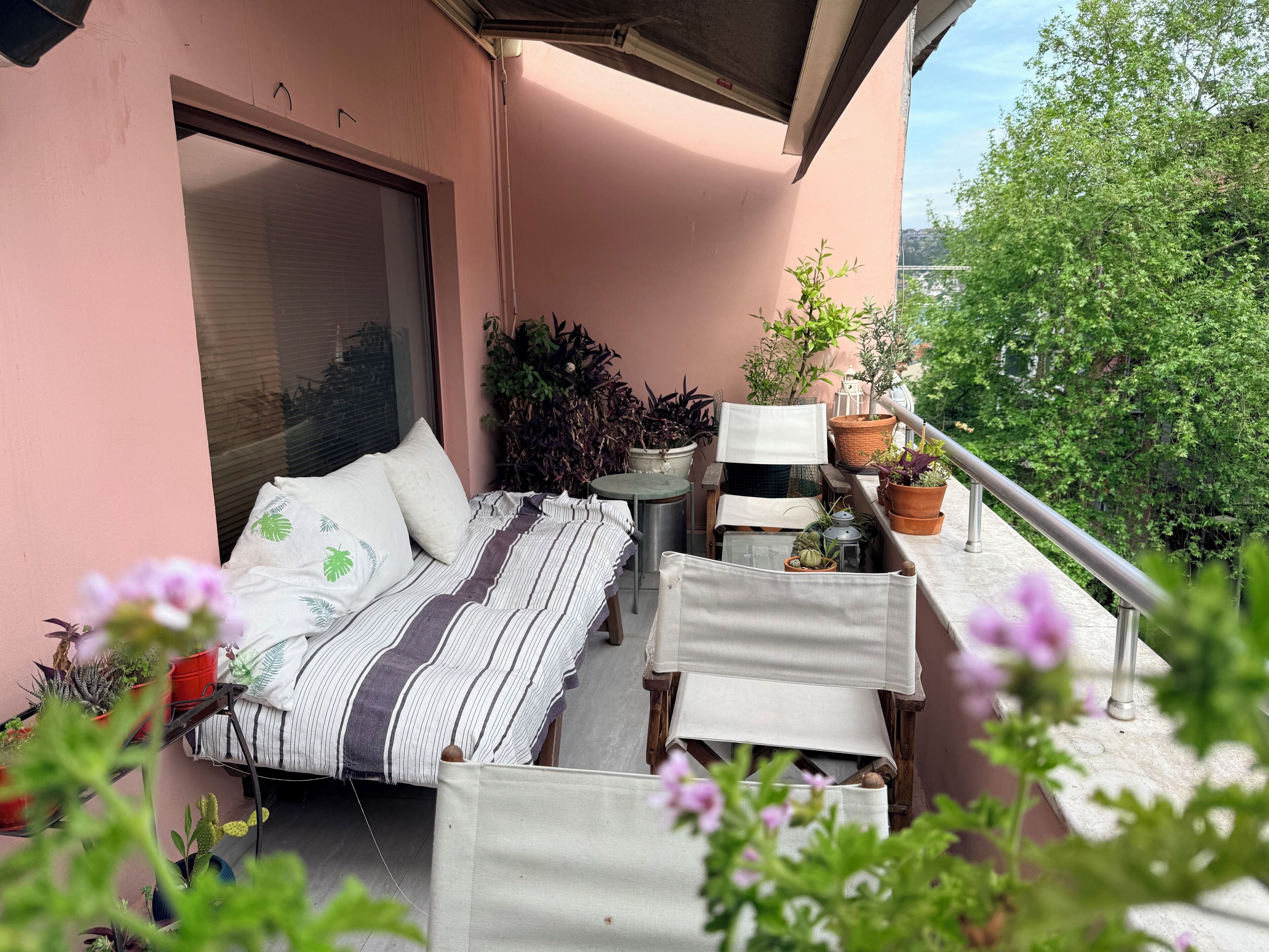 A balcony with a bed, potted plants, and a railing.