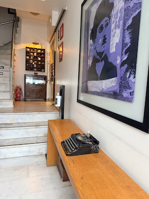 Eine Treppe führt zu einer zweiten Etage, eine Holzbank mit einer Schreibmaschine, ein an der Wand befestigtes Regal mit Dekorationen und ein gerahmtes Kunstwerk.
