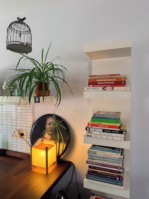 Ein Zimmer mit Bücherregal, Topfpflanze, Pendelleuchte und Spiegel an der Wand.