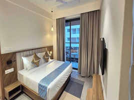 Habitación de hotel con cama, televisión, ventana con cortinas y vistas al exterior.