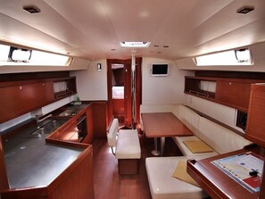Cocina compacta con lavamanos, estufa y armarios de almacenamiento. Hay una pequeña zona de estar con cojines y una mesa.
