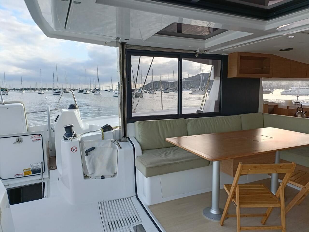 Interior de un barco con comedor, una pequeña mesa y vista al puerto deportivo.