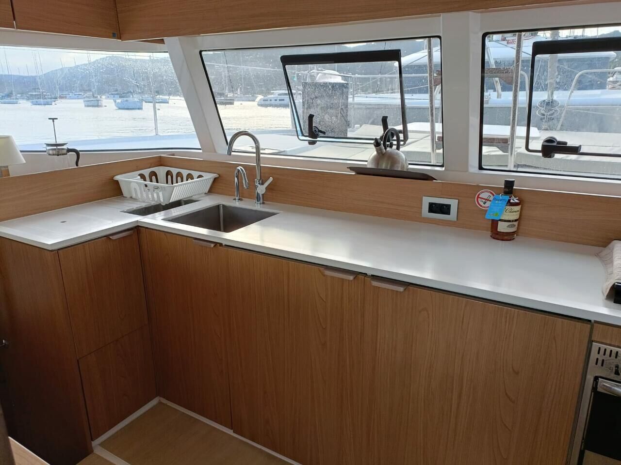 Una piccola cucina lineare con lavandino, pensili e oblò che offre vista sul porto turistico.