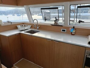 A compact galley with a sink, storage cabinets, and a window providing a view of the marina.