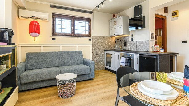 A compact living space with a sofa, dining table, kitchen area, and a small side table. - Secret Rooftop Suite – Tor Vergata Metro (Roma)