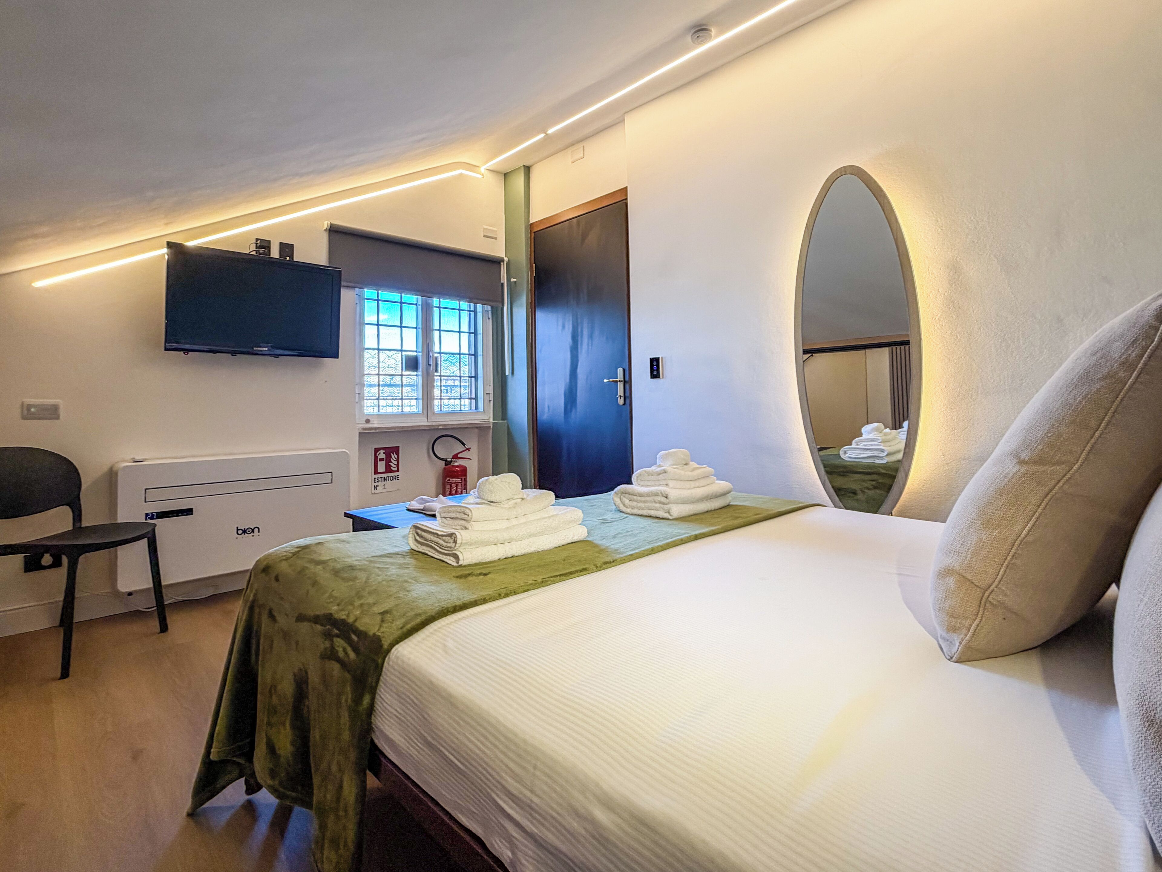 Habitación de hotel con cama, escritorio, silla, televisor de pantalla plana, ventana con vistas y espejo.