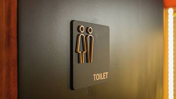 Ein WC-Schild mit Männlein- und Weiblein-Symbol und dem Wort 'TOILET' an einer dunklen Wand.