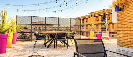Un área de patio al aire libre con una mesa redonda, sillas, luces colgantes y plantas en macetas.