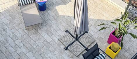 A rooftop terrace with a seating area, a table with drinks, a large umbrella, and potted plants.