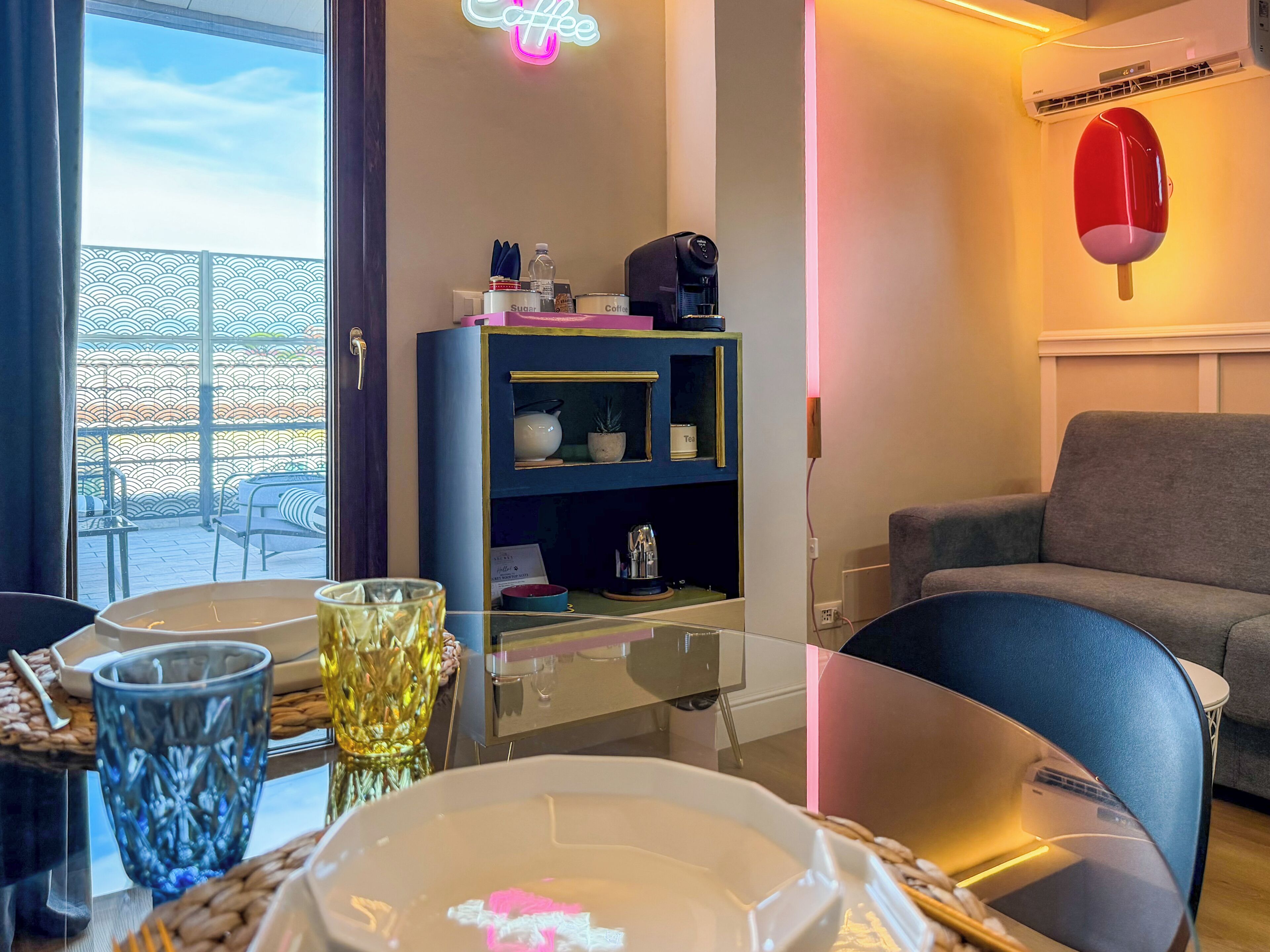 Una sala de estar moderna con una mesa de vidrio, un sofá, una estantería decorativa y un letrero de neón.