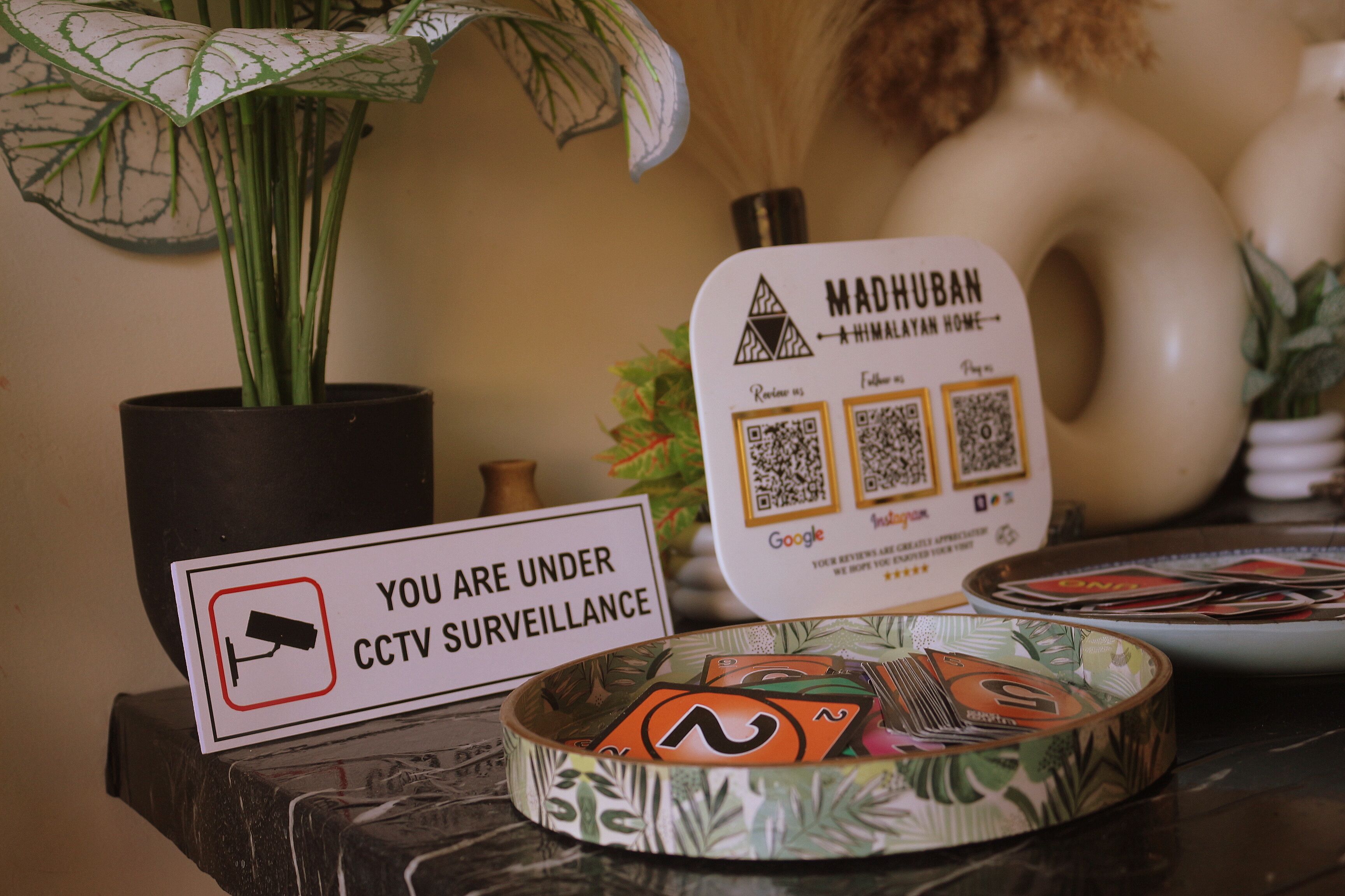 Una mesa con un cartel que indica vigilancia por cámaras CCTV, un código QR para dejar una reseña y un cuenco decorativo con una planta.