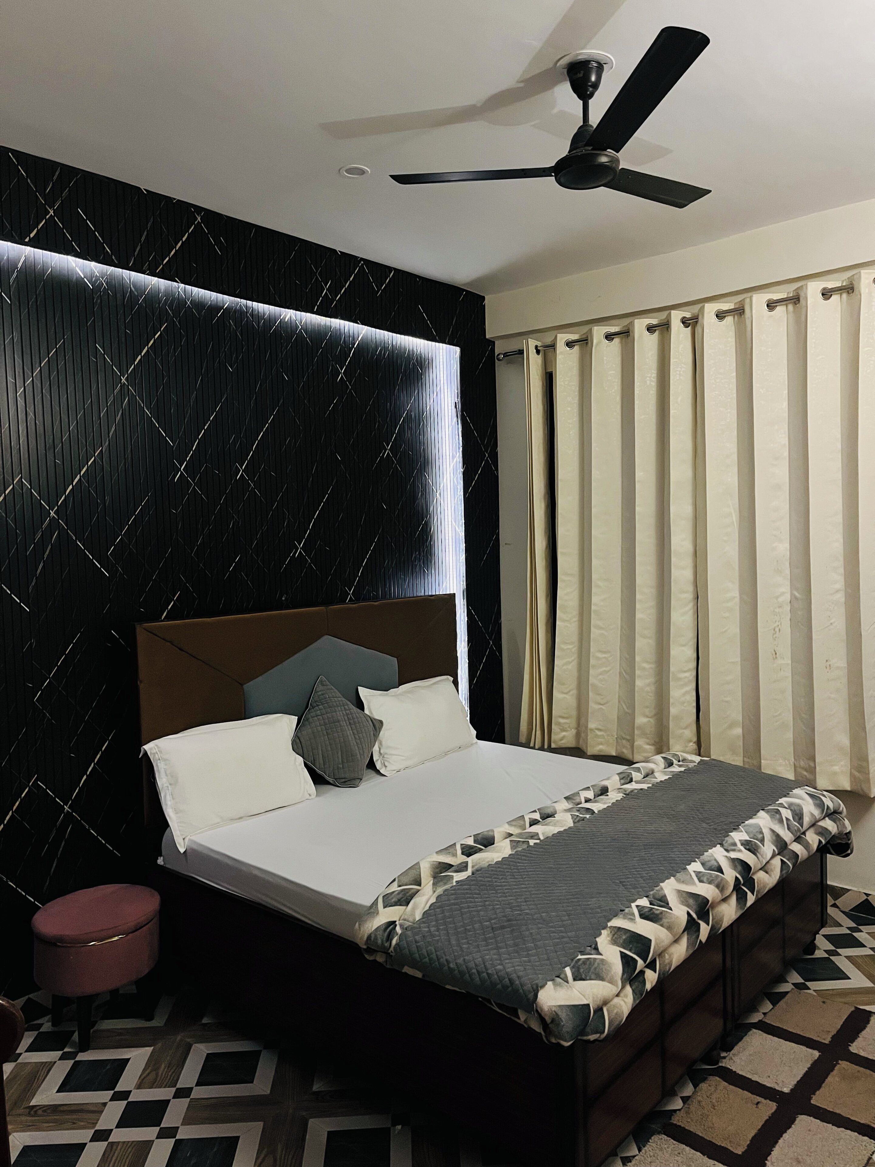 A bedroom with a bed, a ceiling fan, a window with curtains, and a patterned floor.