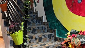 A staircase with stone steps, a green bucket with plants, and a large decorative wall with a circular design.