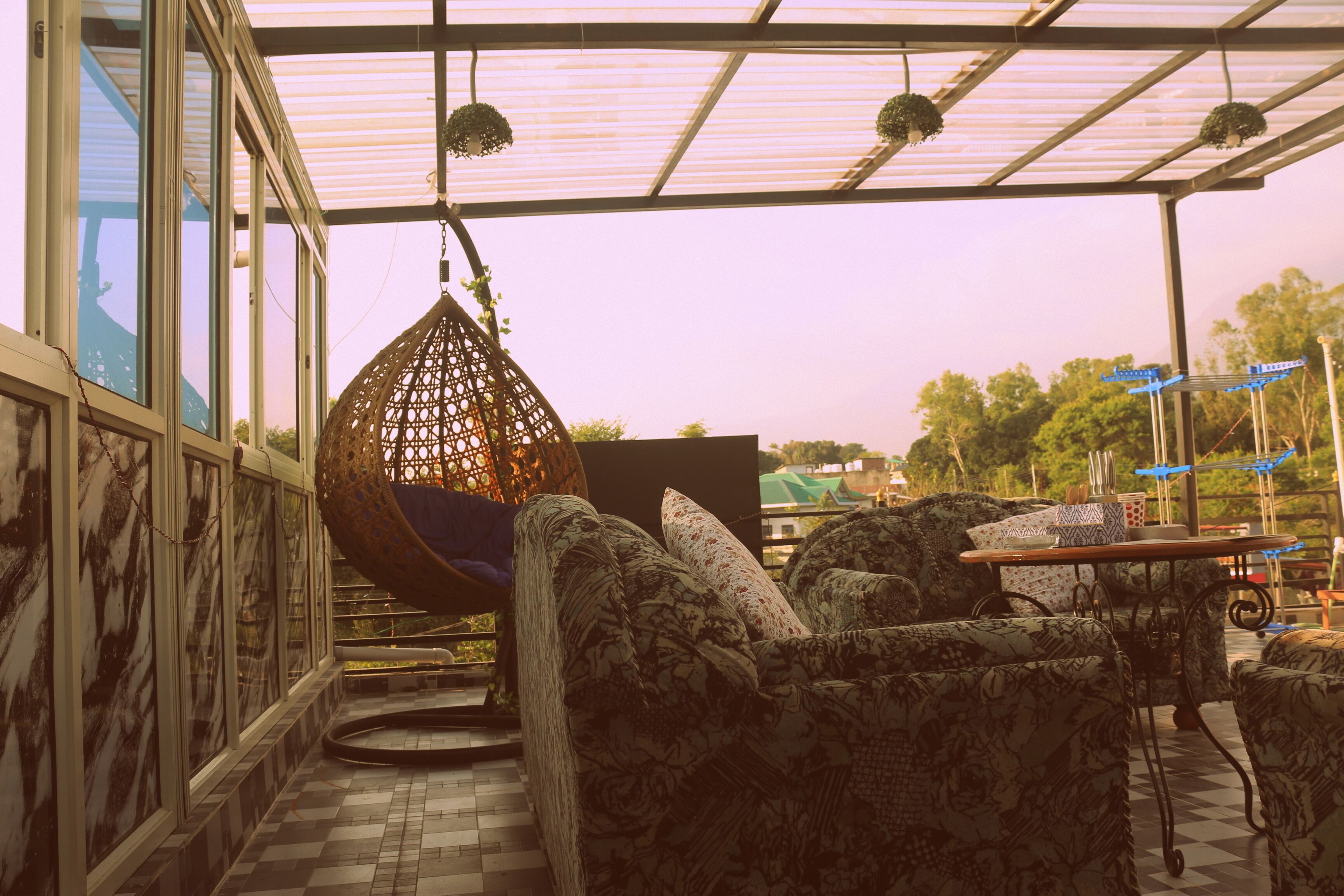 A covered outdoor seating area with patterned furniture, a hanging chair, and a table with items on it.