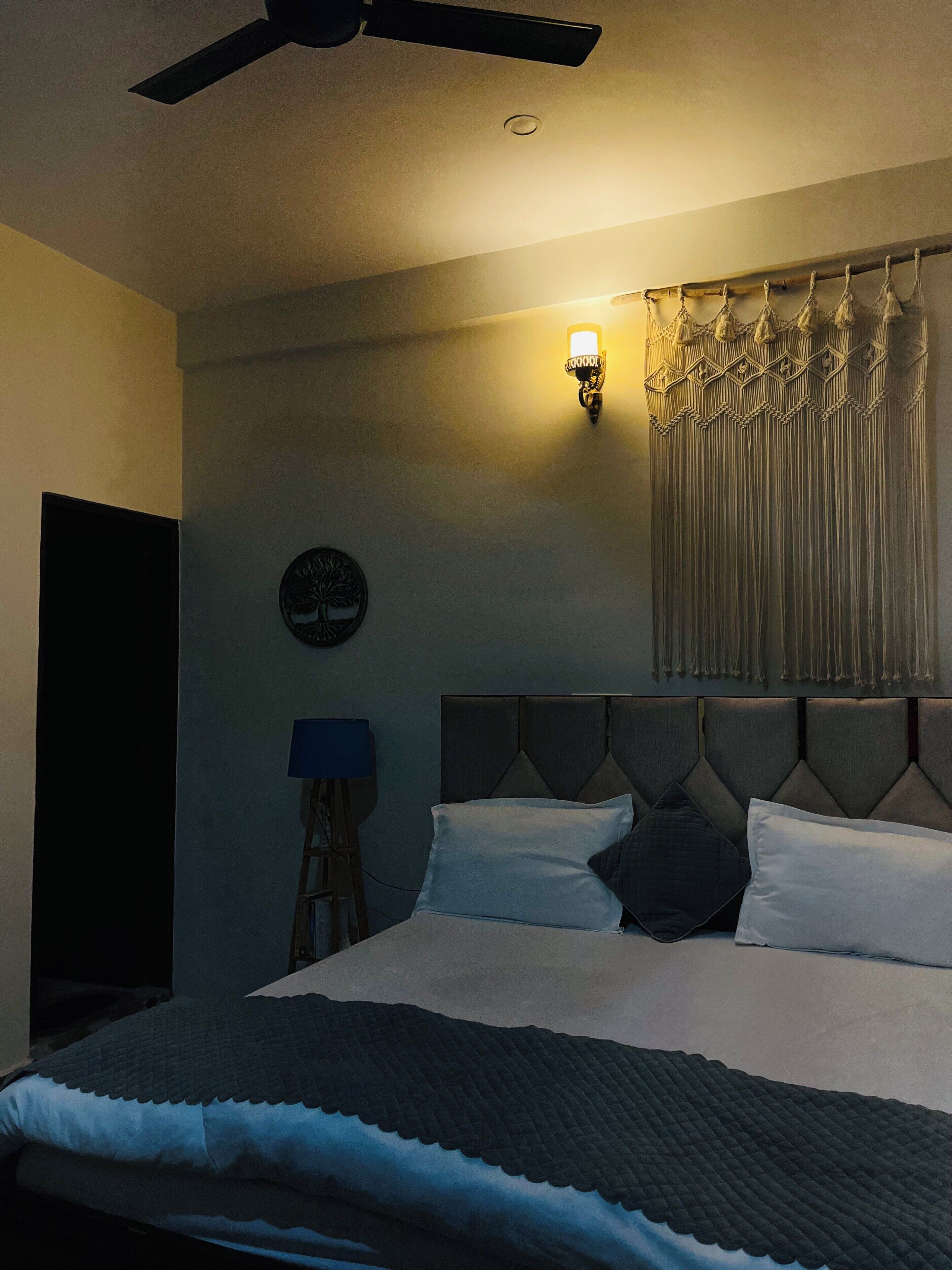 Un dormitorio con cama, ventilador de techo, lámpara de pared y cortina.