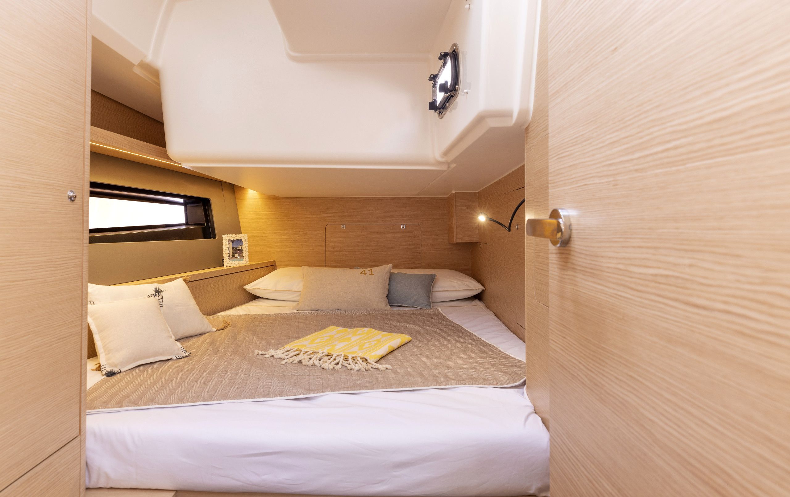 A compact, well-lit cabin with a single bed, a small window, and a wall-mounted light fixture.