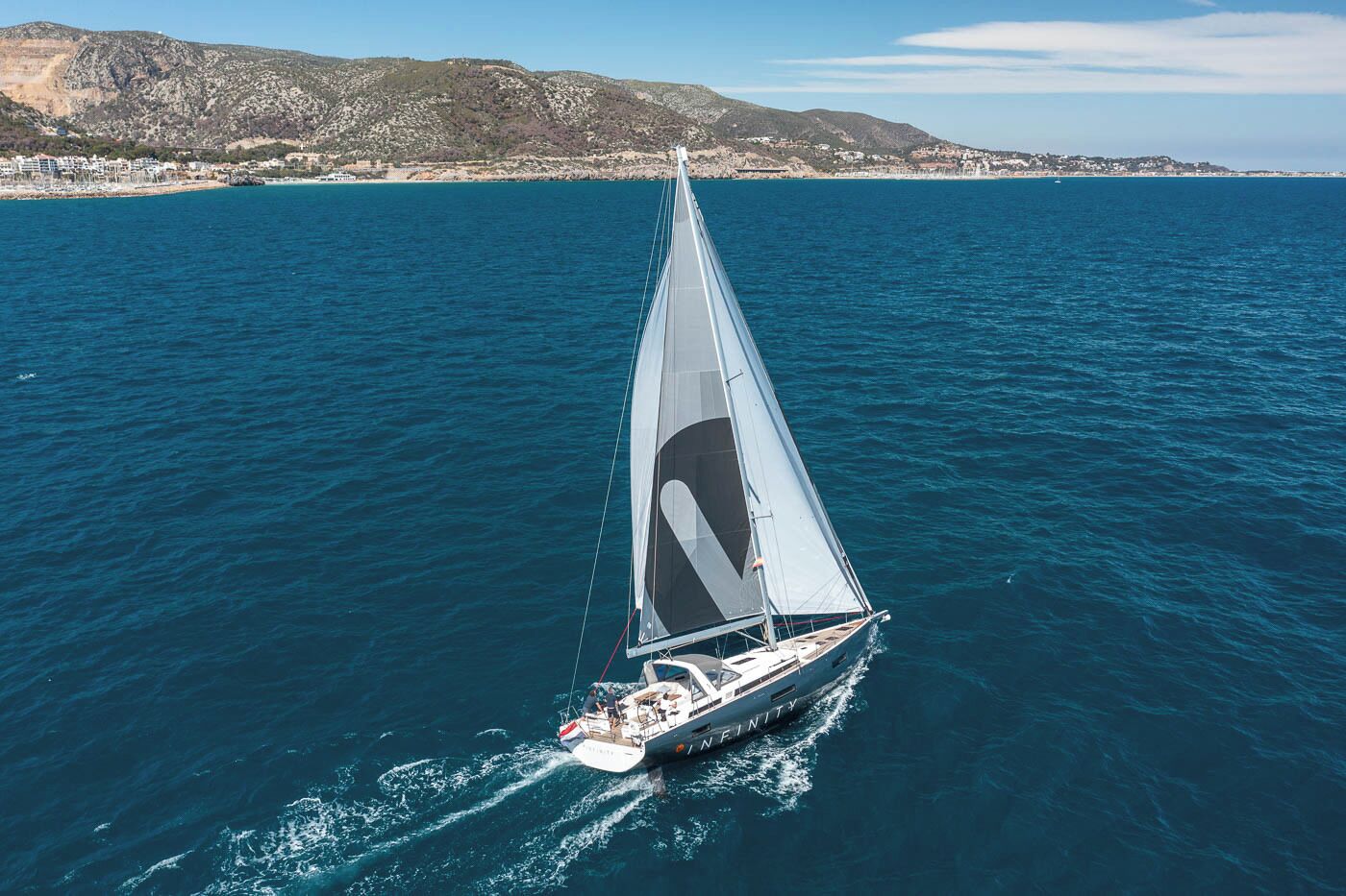 A sailboat named 'INFINITY' on a body of water with a coastal landscape in the background.