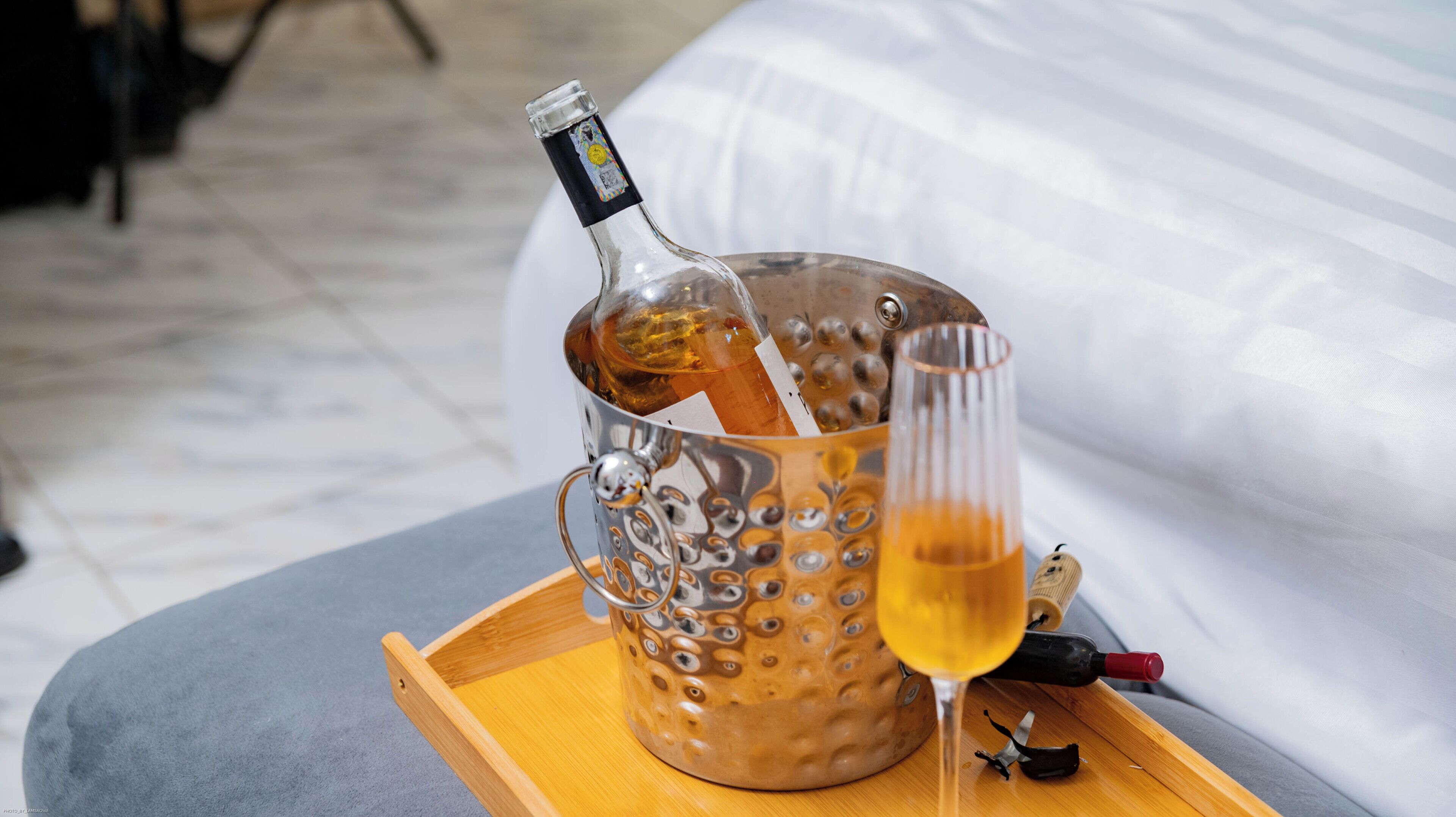 A bottle of champagne in a metallic bucket with a glass of champagne on a tray.