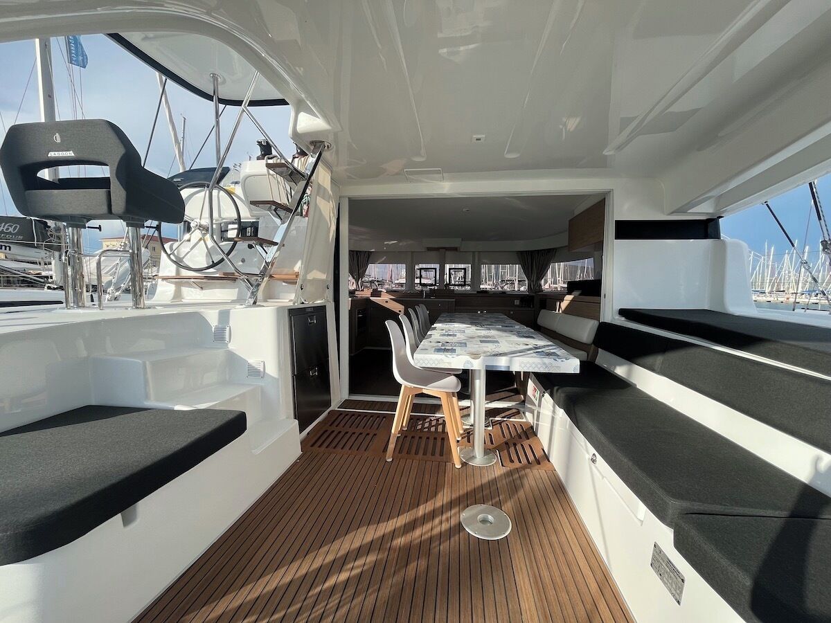 A boat's deck with a table and chairs, a steering wheel, and a view of the marina.