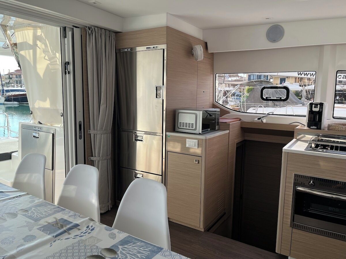 A compact kitchen with a refrigerator, microwave, and oven, a dining area with chairs, and a view of the marina through the window.