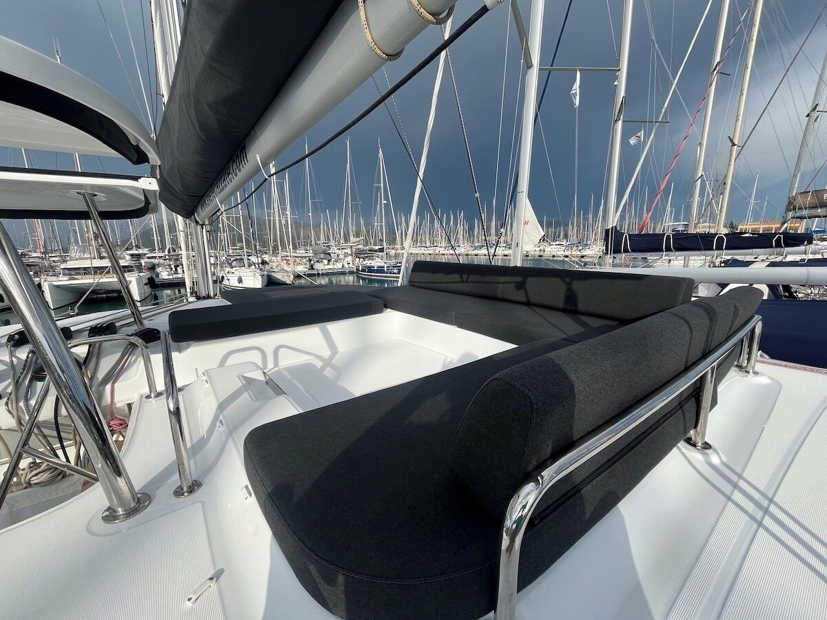 A boat deck with a cushioned seating area, metal railings, and a view of other boats in the marina.