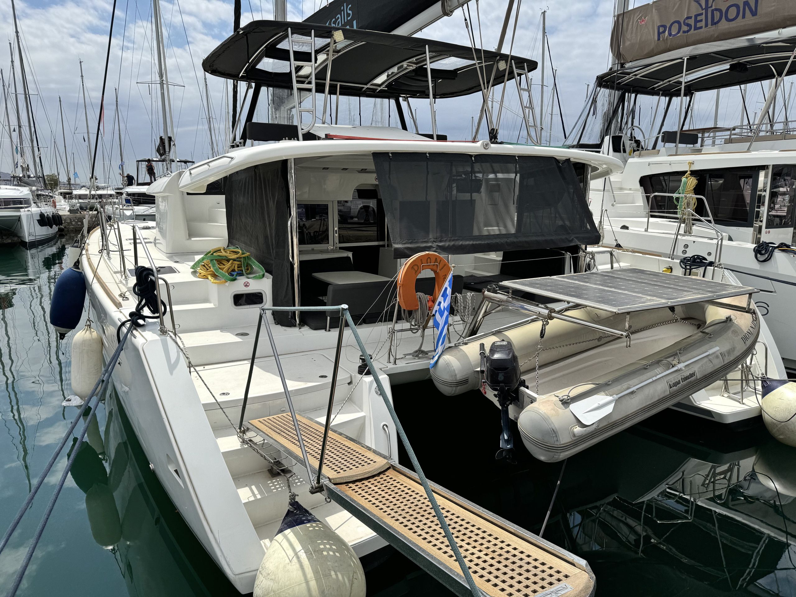 A marina with multiple sailboats docked, featuring lifeboats, a covered seating area, and a solar-powered charging station.